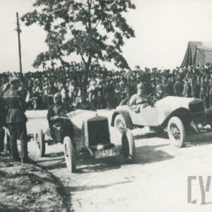 tłum widzów obserwujący wyścig dwóch samochodów sportowych prowadzonych przez mężczyzn w strojach kierowców wyścigowych