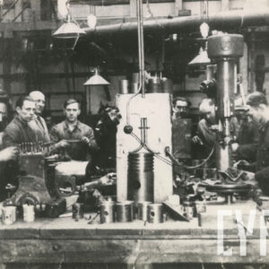 grupa mężczyzn w strojach roboczych stojąca przy stole z maszynami i narzędziami