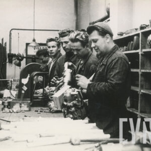 grupa mężczyzn w średnim wieku w ubraniach roboczych stojąca przy stanowisku pracy ze sprzętem mechanicznym