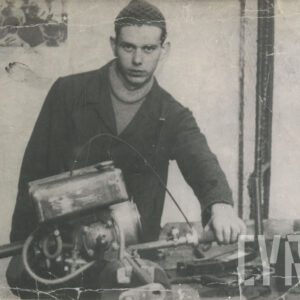 młody mężczyzna w stroju roboczym, pozujący do fotografii przy silniku położonym na stole