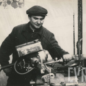 mężczyzna w stroju roboczym, pozujący do fotografii przy silniku położonym na stole