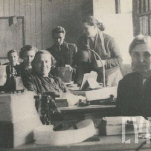 grupa kobiet i jeden mężczyzna siedzący przy biurkach, pozujący do fotografii