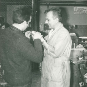 dwóch mężczyzn w ubraniach roboczych trzymających metalowy przedmiot