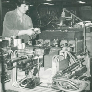 kobieta w średnim wieku w ubraniu roboczym, pracująca przy urządzeniu mechanicznym