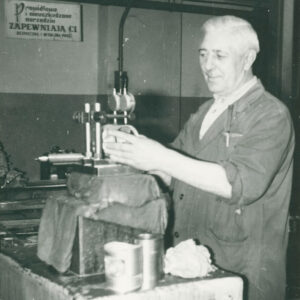 starszy mężczyzna w ubraniu roboczym, stojący przy stanowisku z urządzeniem mechanicznym