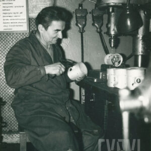 starszy mężczyzna w ubraniu roboczym, siedzący przy stanowisku z wiertarką