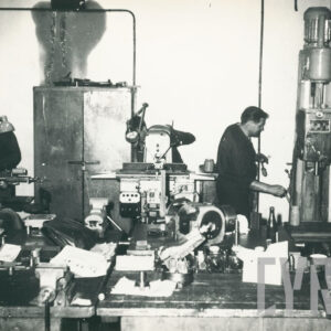 grupa osób w strojach roboczych, pracująca przy maszynach mechanicznych