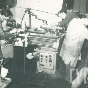 grupa osób w strojach roboczych, pracująca przy maszynach mechanicznych