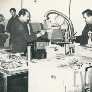 grupa osób w strojach roboczych, pracująca przy maszynach mechanicznych