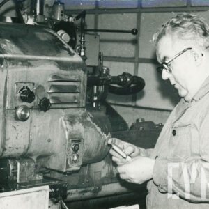 starszy mężczyzna w ubraniu roboczym, pracujący przy stanowisku z maszyną mechaniczną 