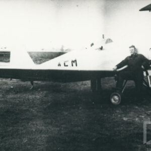 mężczyzna w stroju roboczym opierający się o kadłub samolotu stojącego na trawiastym lądowisku