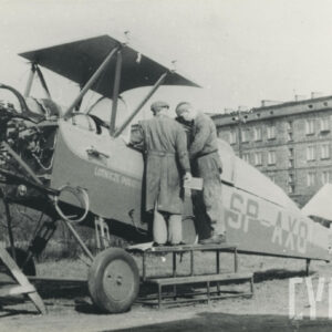 dwóch mężczyzn stojących na podwyższeniu i zaglądających do wnętrza samolotu, w tle blok mieszkalny