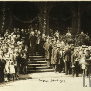 duża grupa ludzi stoi po obu stronach schodów, u szczytu których stoi mężczyzna w surducie na tle ozdobionych girlandami arkad 