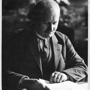 mężczyzna w marynarce pod krawatem siedzi przy biurku i przegląda dokumenty