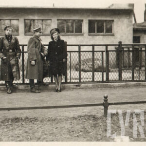 troje dorosłych ludzi, dwóch mężczyzn i kobieta, stoją przed metalowym ogrodzeniem wybiegu dla hipopotama, w głębi fragment budynku i leżący hipopotam