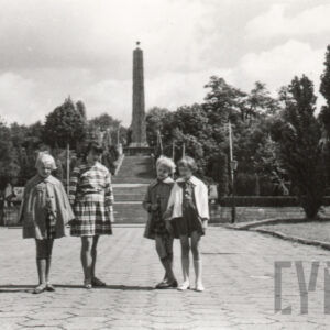 cztery małe dziewczynki w sukienkach lub spódniczkach stoją na tle wysokich schodów prowadzących do strzelistej iglicy pomnika zakończonego gwiazdą