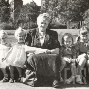 starsza pani siedzi z czterema małymi dziewczynkami na obmurowaniu stawu przed Operą