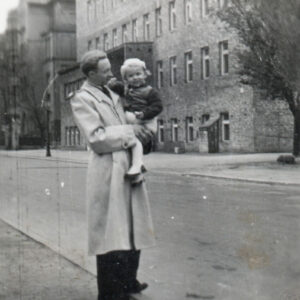 mężczyzna z małą dziewczynką na rękach stoi na krawędzi ulicy, w głębi nieotynkowany budynek