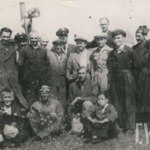 grupa osób, część ubrana w stroje robocze, jeden w ubranie pilota, pozująca do fotografii