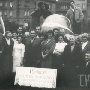 grupa osób - mężczyzn i kobiet, pozujących do fotografii przy samolocie stojącym na tle budynków mieszkalnych