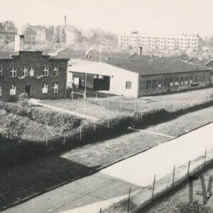 budynki przemysłowe przy niedużej ulicy; w głębi kamienice i blok mieszkalny