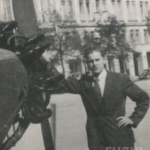 młody, elegancko ubrany mężczyzna w garniturze, koszuli i krawacie, pozujący do fotografii przy silniku samolotu