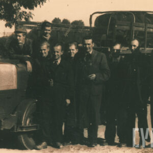 grupa mężczyzn w strojach roboczych, pozujących do fotografii obok pojazdu mechanicznego 