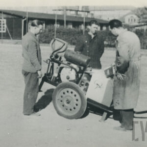 trójka mężczyzn w strojach roboczych stojąca przy urządzeniu mechanicznym na hangarów