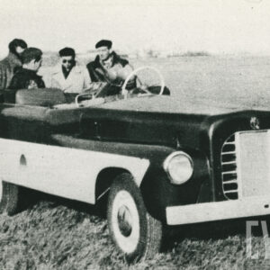 grupa osób w strojach roboczych pozująca do fotografii przy pojeździe mechanicznym na trawiastym lądowisku