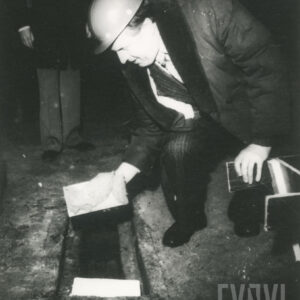 mężczyzna w średnim wieku z kaskiem budowlanym na głowie trzymający kielnie z zaprawą nad przygotowanym wgłębieniem