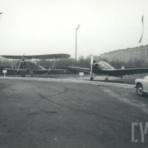 samoloty stojące na wolnej przestrzeni, w tle budynki mieszkalne z cegły