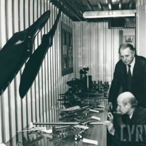 dwóch mężczyzn w garniturach pochylających się nad stołem z modelami samolotów