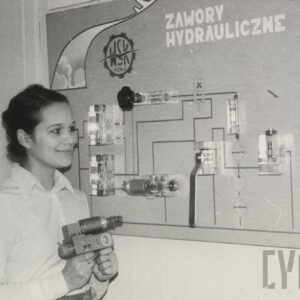 młoda kobieta trzymająca metalowy przedmiot i stojąca przy planszy wiszącej na ścianie