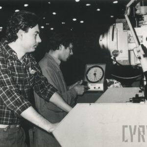 dwóch mężczyzn w strojach roboczych stojących przy maszynie