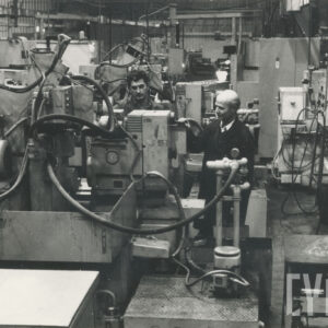 dwóch mężczyzn w strojach roboczych stojących w pomieszczeniu pełnym maszyn i urządzeń technicznych