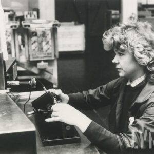 kobieta w stroju roboczym, siedząca przy biurku, na którym stoją urządzenia mechaniczne