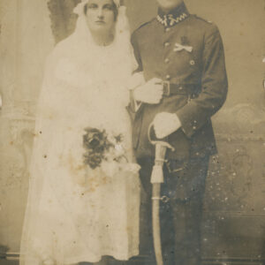 mężczyzna w mundurze wojskowym i szablą w dłoni pozujący do fotografii z kobietą w sukni ślubnej, trzymającą w ręku bukiet kwiatów
