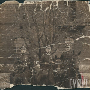 trzech mężczyzn w mundurze siedzących na koniach, na tle ceglanego budynku