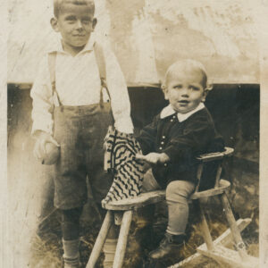 dwóch chłopców pozujących do zdjęcia; jeden z nich stoi i w ręku trzyma piłkę, a drugi siedzi na bujanym koniu