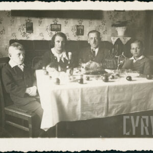 mężczyzna i kobieta w średnim wieku z dwójką młodych chłopców, wszyscy elegancko ubrani siedzą przy zastawionym stole i pozują do fotografii