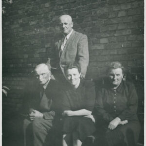 dwóch mężczyzn i dwie kobiety pozujący do fotografii na tle budynku z cegieł, jeden mężczyzna stoi, pozostali siedzą