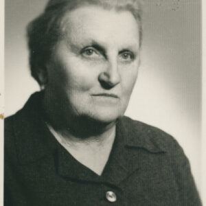 popiersie starszej kobiety o siwych włosach zaczesanych do góry pozującej do fotografii, na dekolcie kołnierzyk ciemnej sukienki lub garsonki zapinanej na widoczny guzik