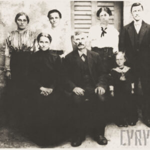 siedem elegancko ubranych osób pozujących do fotografii na tle budynku z okiennicami