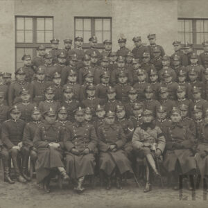 duża grupa młodych mężczyzn w mundurach i czapkach wojskowych pozująca do pamiątkowej fotografii na tle ceglanego budynku