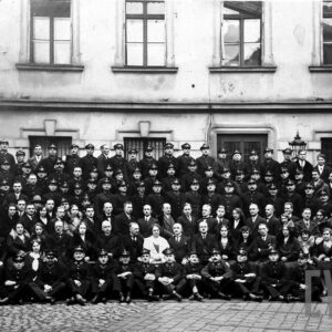 grupa kilkudziesięciu osób ustawionych w sześciu rzędach, głównie mężczyzn w mundurach pocztowych, pozujących do fotografii na tle budynku 