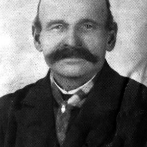 starszy, łysy mężczyzna z wąsami, ubrany elegancko w koszulę, krawat i marynarkę