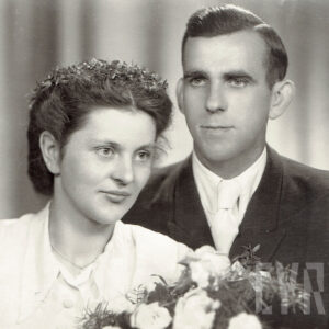 mężczyzna w garniturze z kobietą w sukni ślubnej, trzymającą w ręku bukiet kwiatów