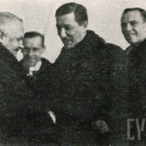 czterech mężczyzn bez nakryć głowy, dwóch z nich wita się podaniem dłoni