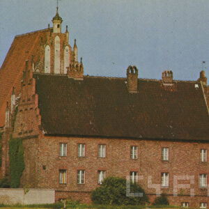 na pierwszym planie ceglany budynek ze spadzistym dachem, za nim wyższy ceglany budynek z wysokim spadzistym dachem zakończonym od frontu małą wieżyczką