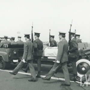 samochód, w którym siedzą żołnierze ciągnie lawetę wojskową na której leży trumna przykryta biało-czerwoną flagą, po obu stronach trumny idą żołnierze 